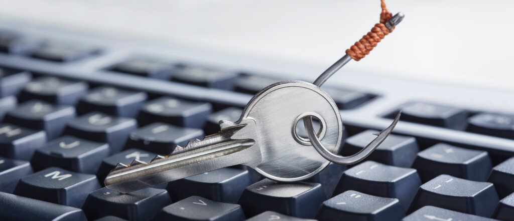 A close-up of a silver key on top of a black keyboard. There is a fishing hook through the key's bow.